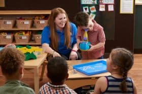 teacher helping preschool student look through a microscope