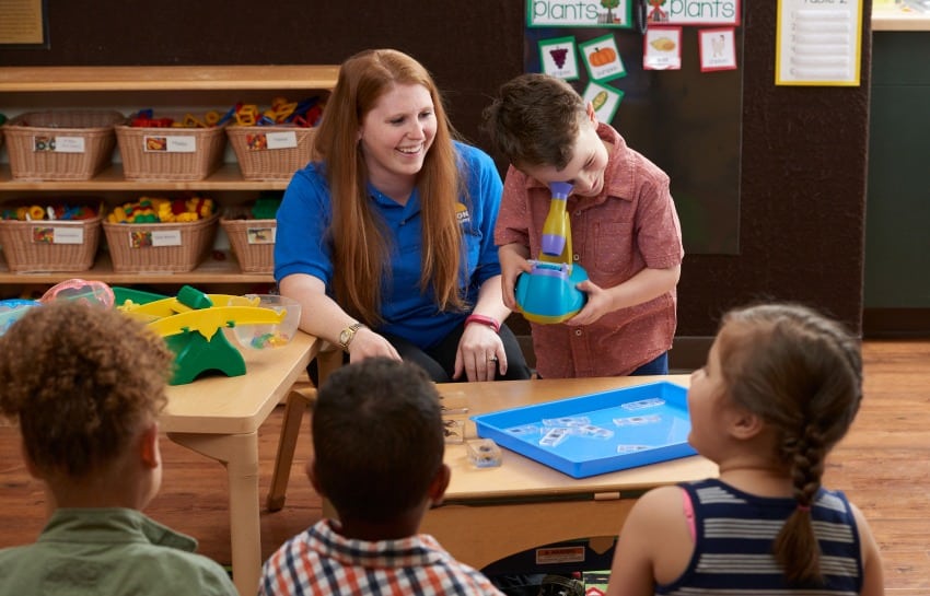 teacher helping preschool student look through a microscope
