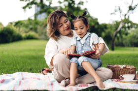 mother reading to preschool child outside in the spring