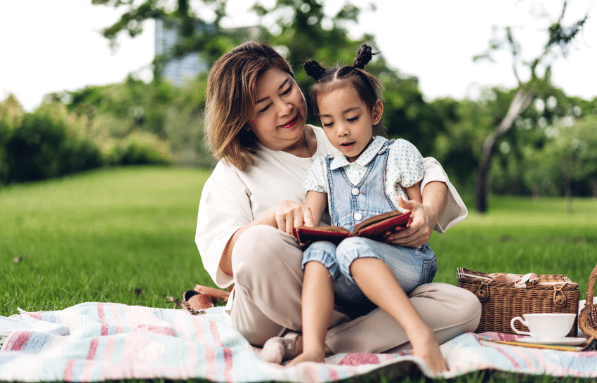 mother reading to preschool child outside in the spring