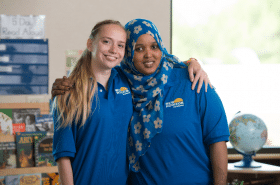 Two New Horizon Academy childcare teachers smiling and hugging while working in a classroom