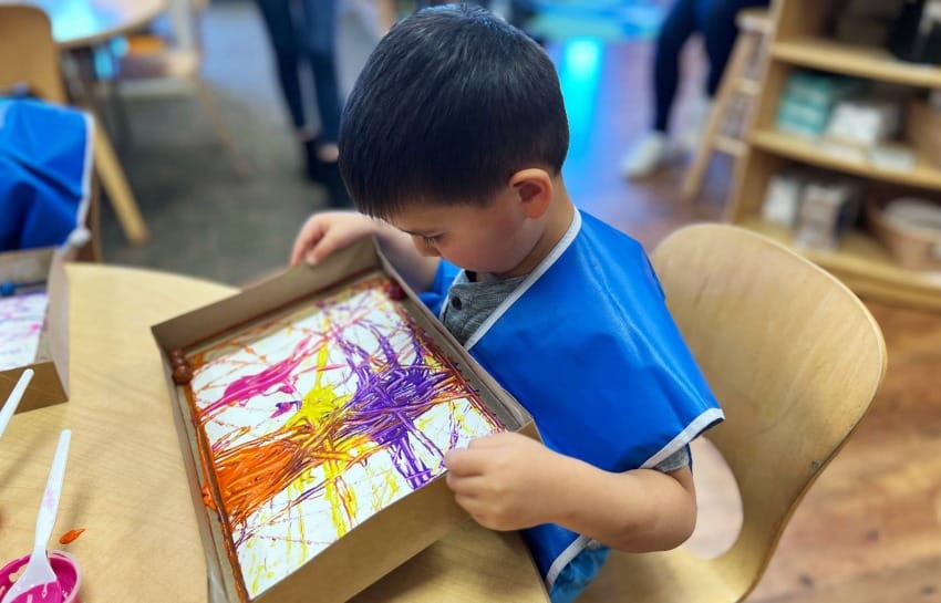 Preschool child rolling marble across painted paper to make marble painting art