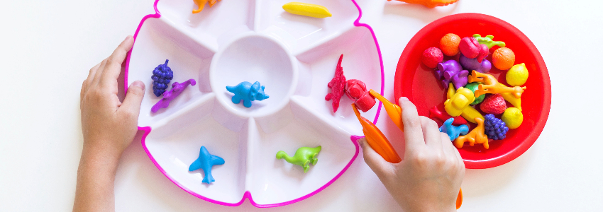 Child practicing fine motor skills by picking up toys with play tongs