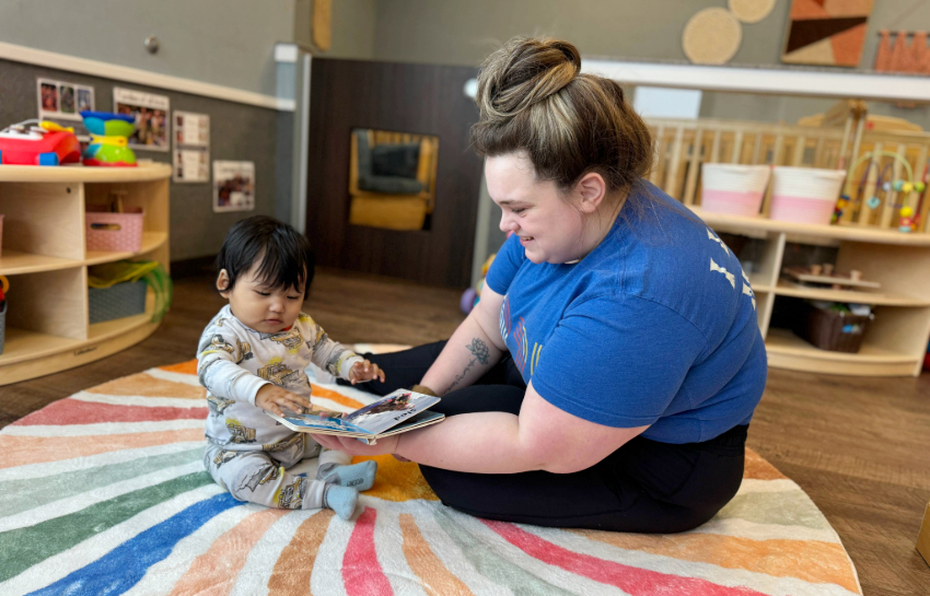 Infant daycare teacher reading a hardcover book to baby